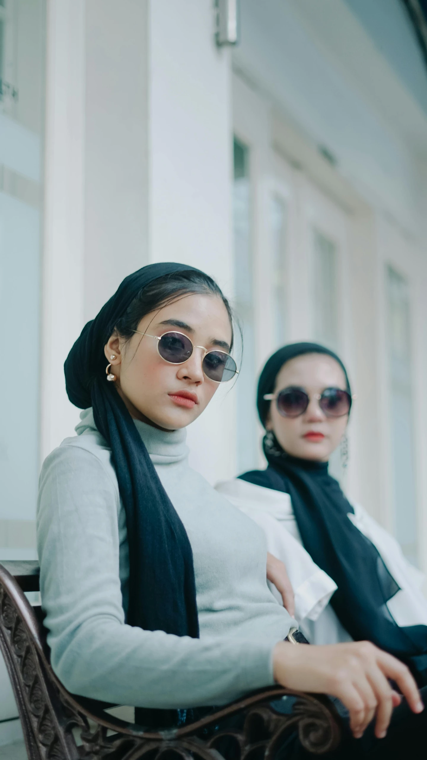 two women sitting outside one has sunglasses and the other has a scarf