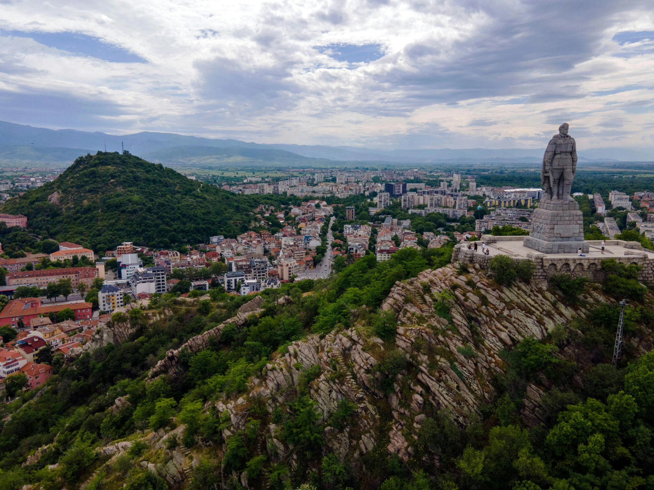 a statue standing on top of a tall mountain next to trees