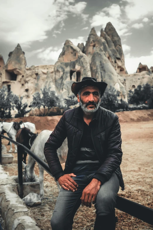 man in cowboy hat sitting on stone ledge with horses behind him