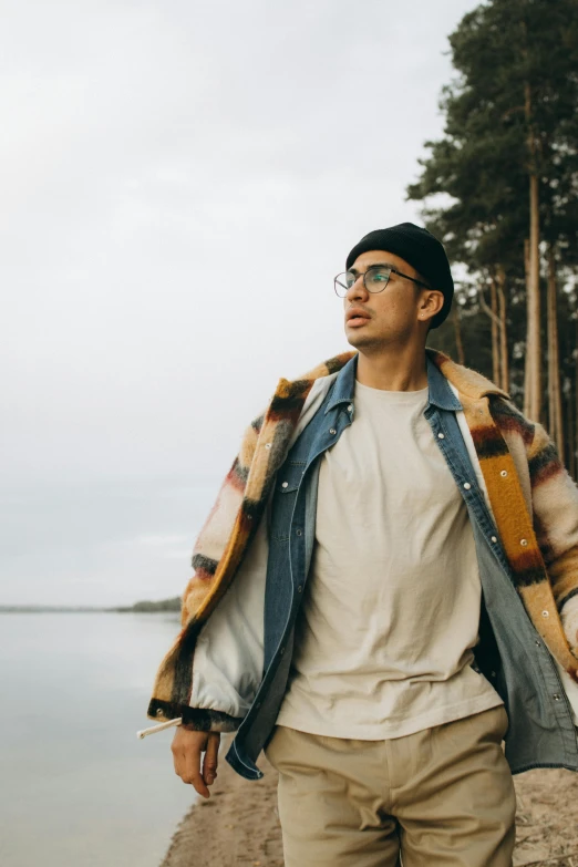 a man with glasses, jacket and jeans walking towards water