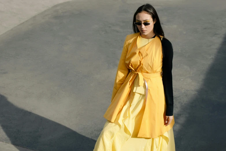 a woman standing on concrete in a long yellow dress