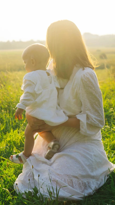 two young women in white dresses are sitting in a field