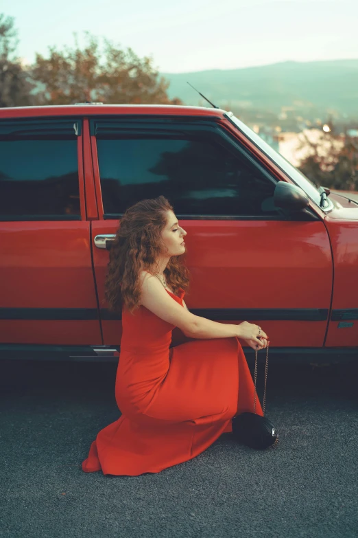 a woman in an orange dress with her hair down sits near her car