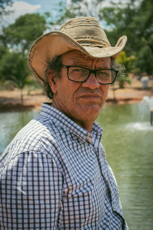 a man wearing a hat and glasses next to a lake