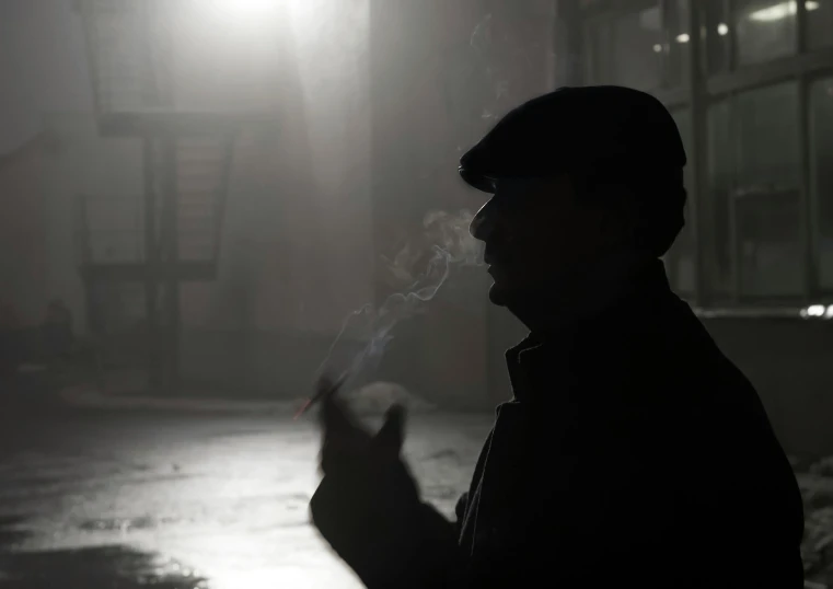 man with a hat standing in the dark smoking