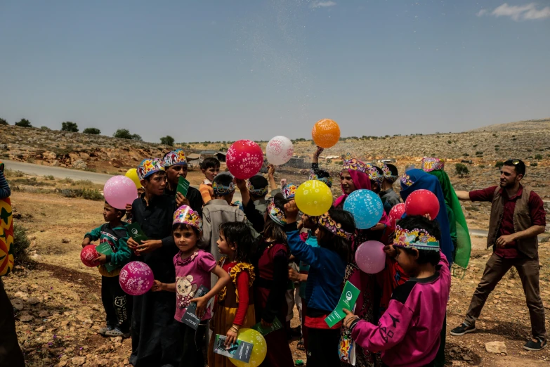 a group of children standing together under helium balloons