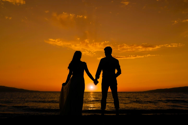 two people hold hands as the sun rises over the ocean