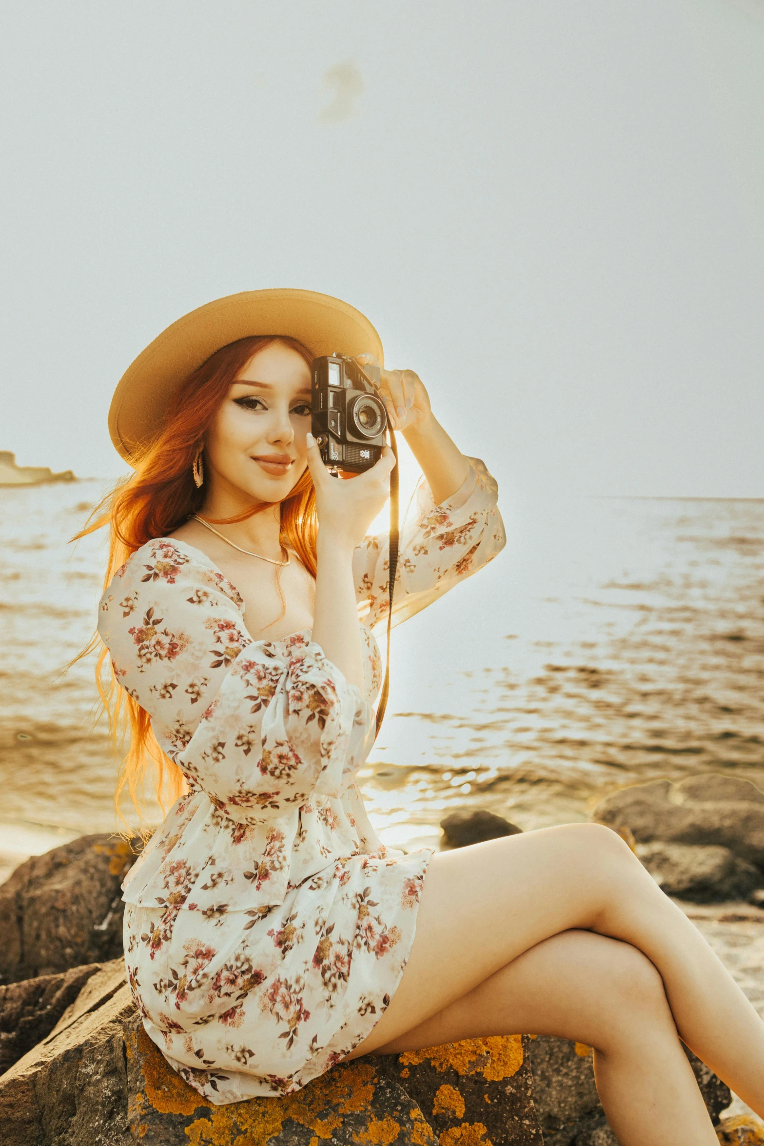 a pretty woman sitting on a rock while holding a camera