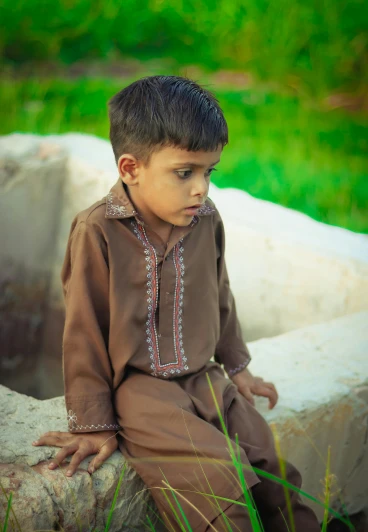 a boy in brown outfit sitting on wall looking at grass