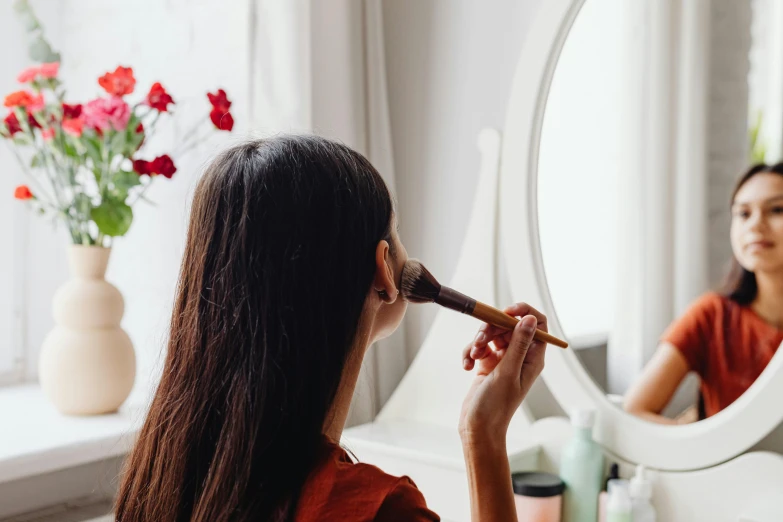 a girl is doing her hair and make - up at the mirror