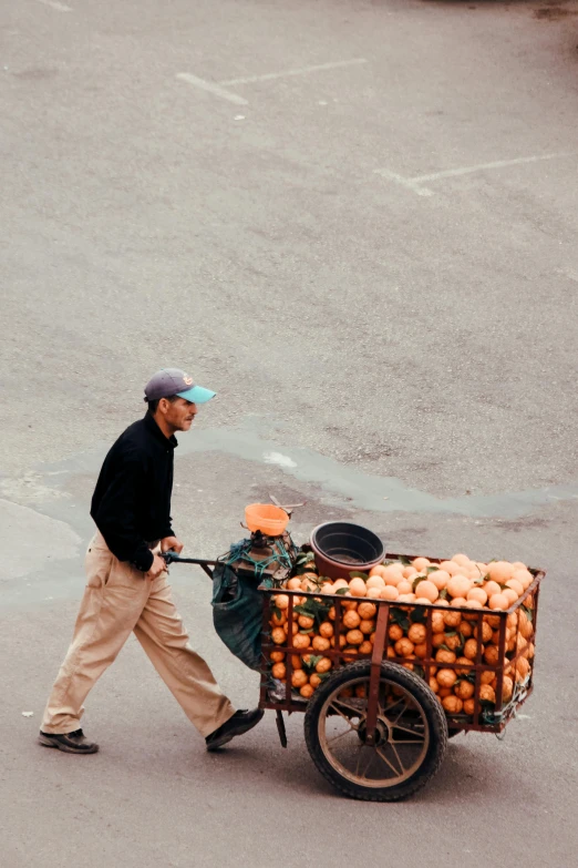 the man walks while hing a large wagon filled with fruit