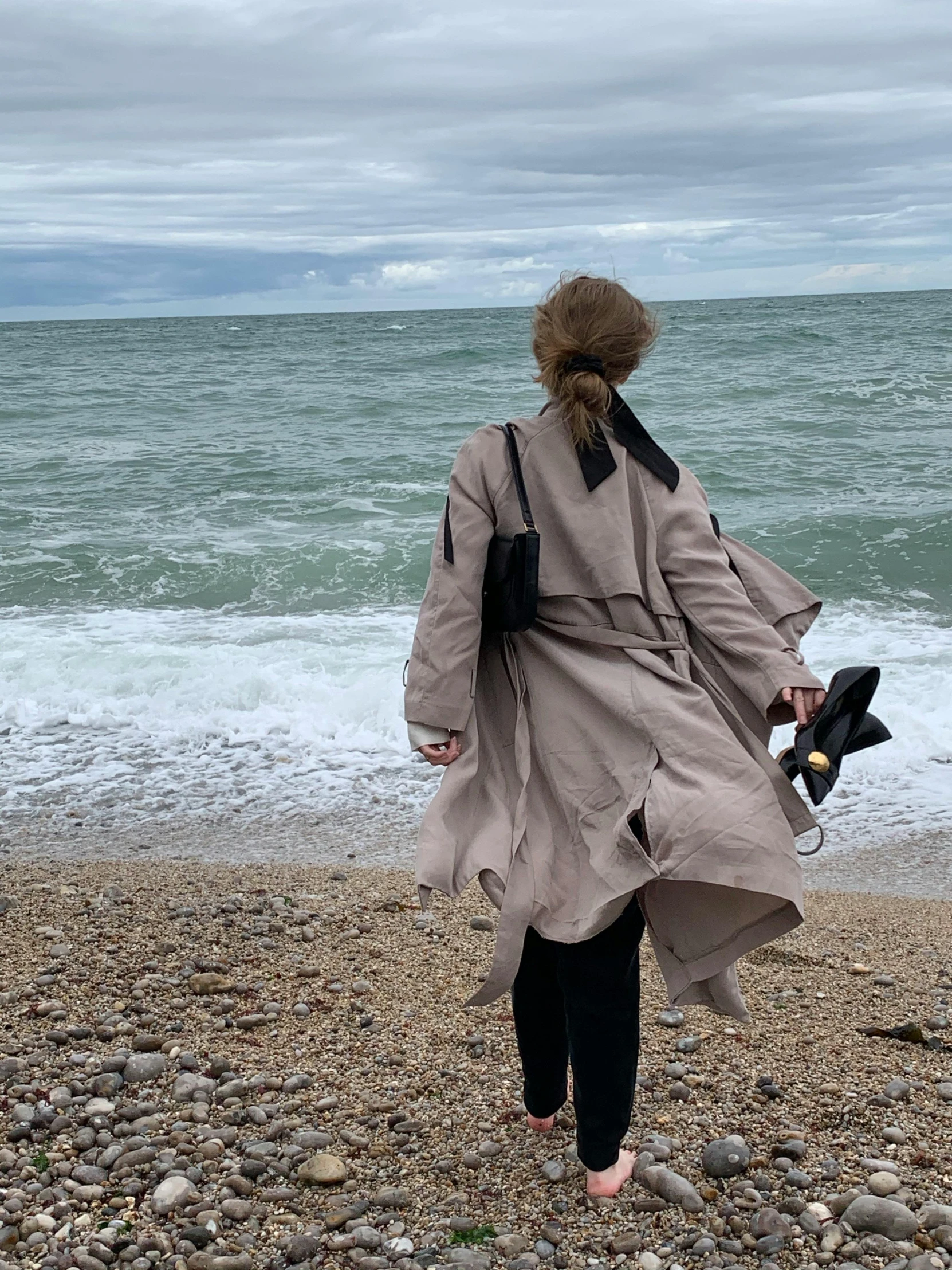 a woman in a gray coat on a beach