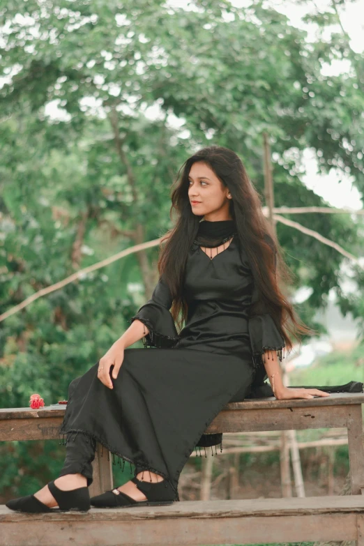 woman in black dress sitting on wooden bench with trees in the background