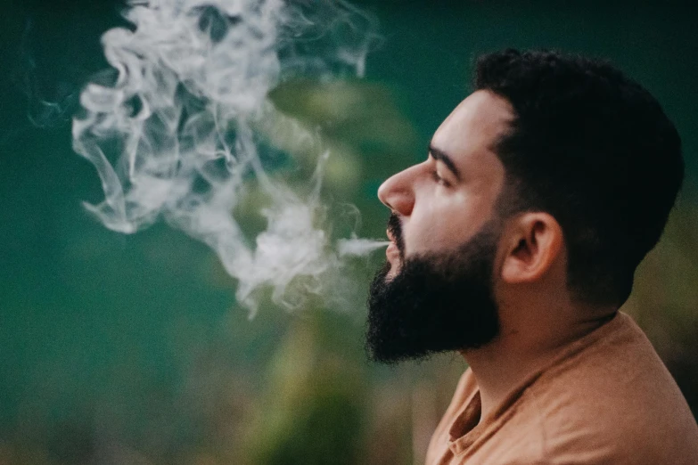 the man smiles while holding his nose up as smoke billows