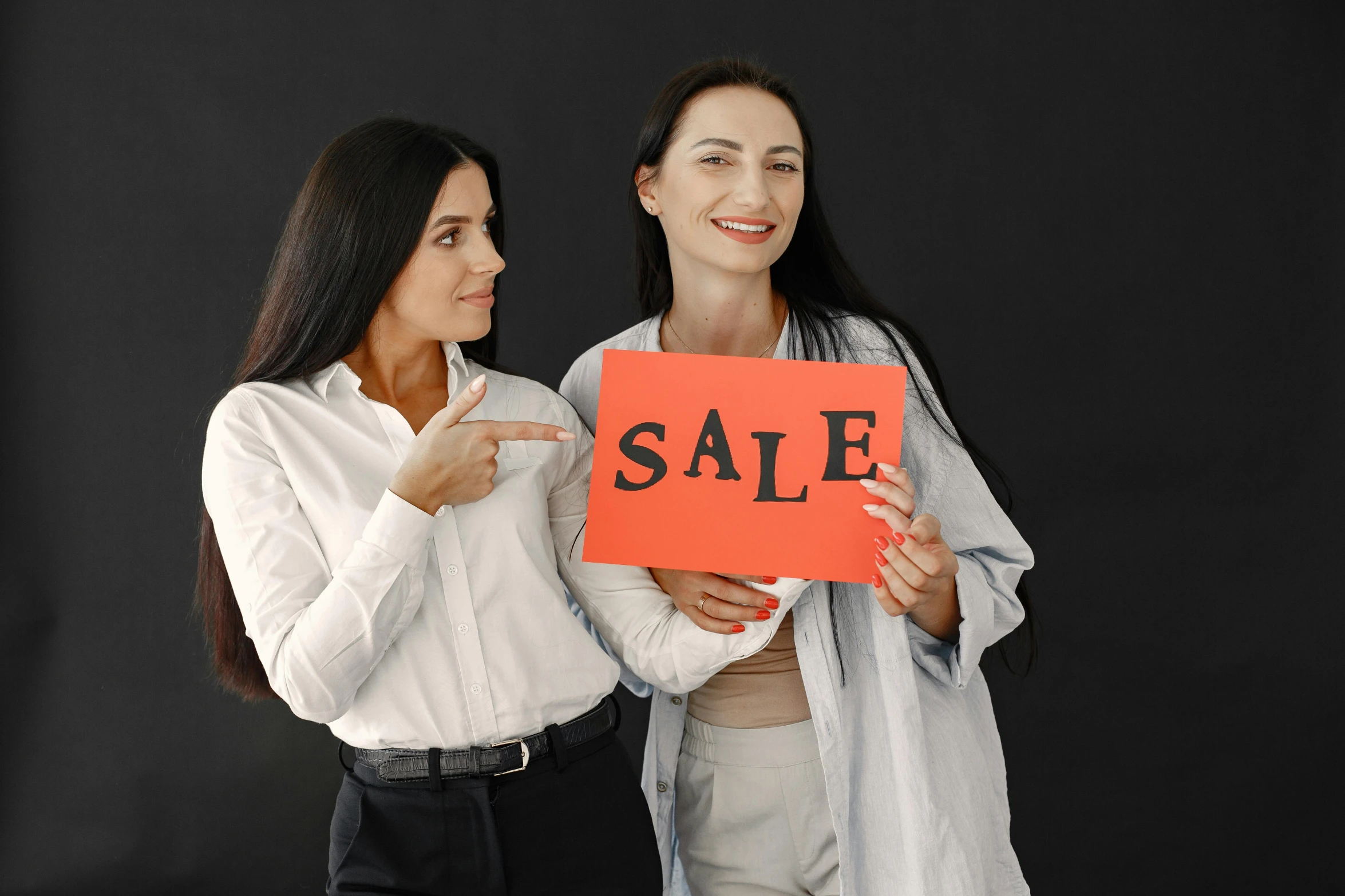 two women holding an orange sale sign in front of their face