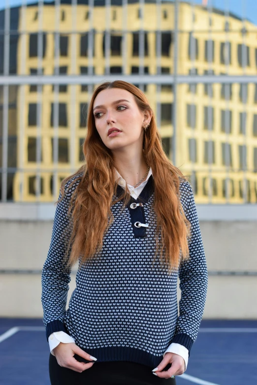 the young red - haired woman in a sweater with long sleeves stands on the parking lot