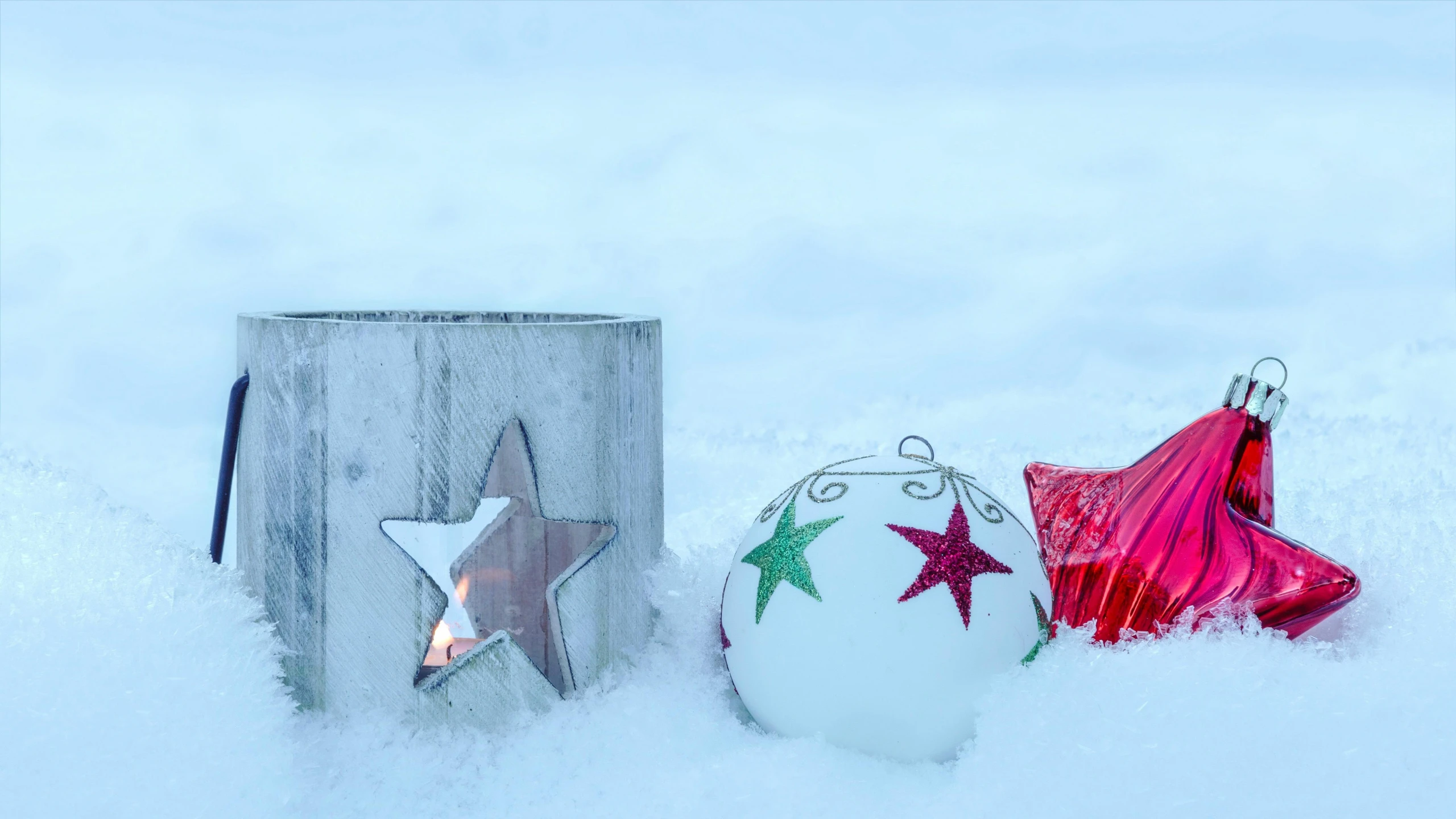 two christmas baubles and an old wooden tin tree ornament are out in the snow