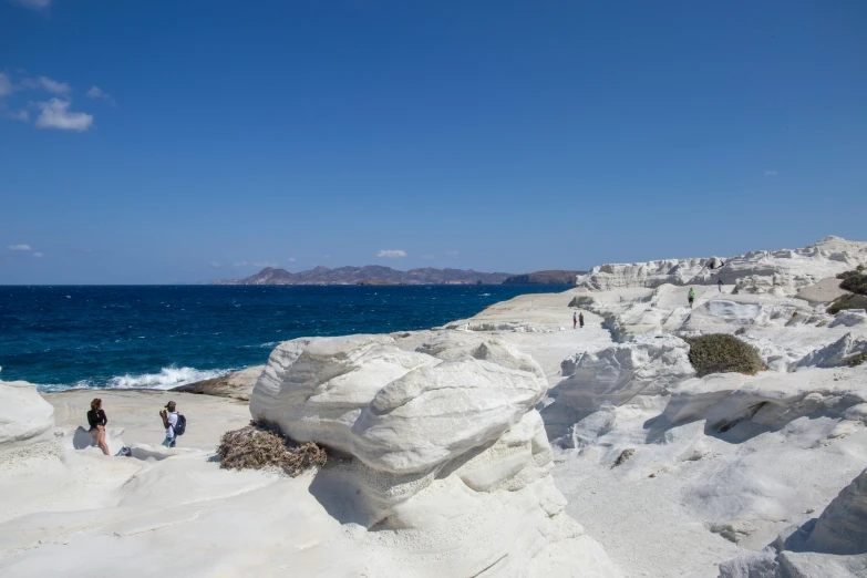 a group of people walking down the sand and rocks of the beach