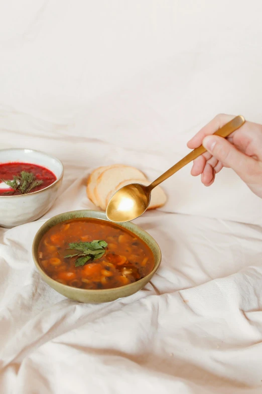 a hand holds a ladle in front of a bowl of soup