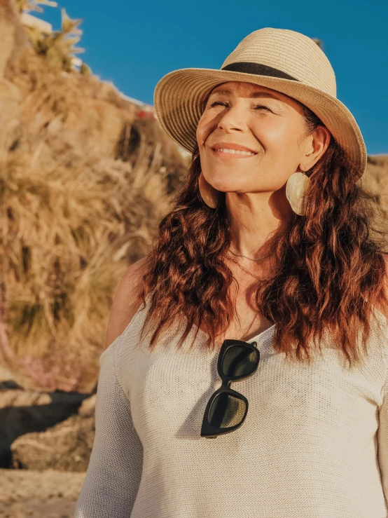 a woman with long curly red hair wearing a hat and smiling