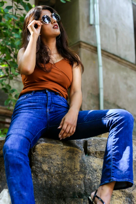 a woman in a tank top and jeans leaning on a rock