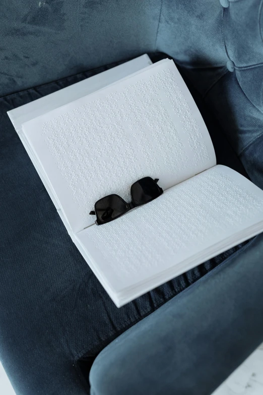 some kind of book sitting on a chair next to a pair of black sunglasses