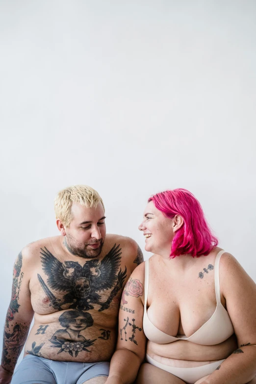 a fat woman and a tattooed man are sitting together