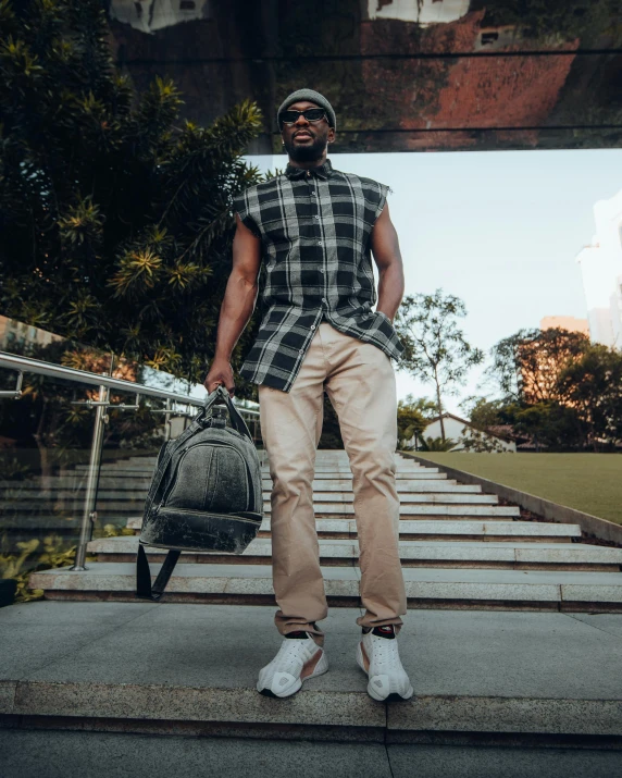 a man in plaid shirt, tan pants, white tennis shoes and a bag