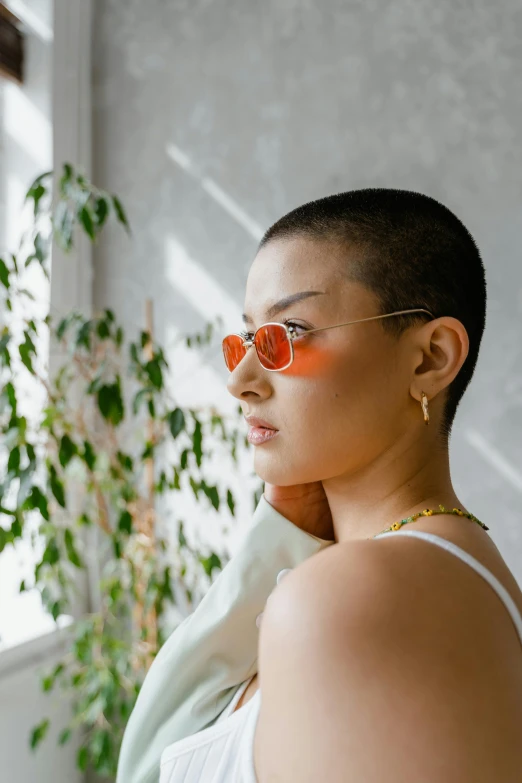 a young woman wearing sunglasses standing in front of a potted plant