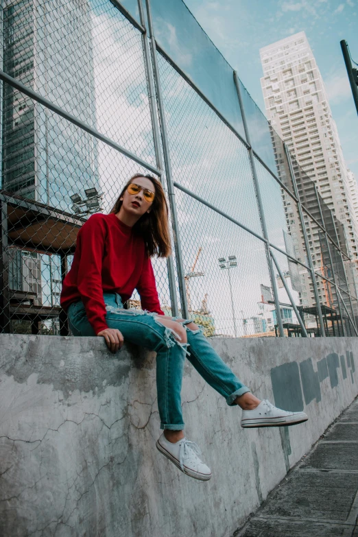 a woman is sitting on a fence next to some tall buildings