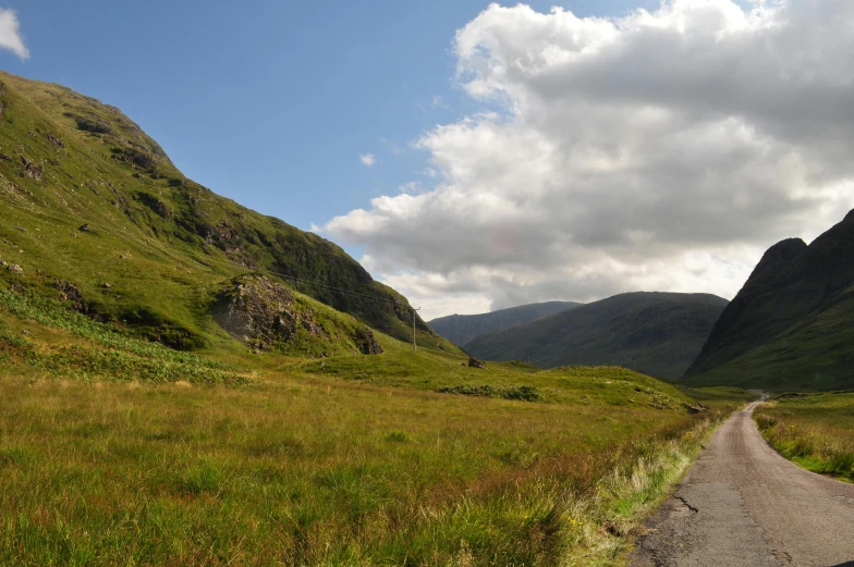 a rural road leads to a grassy valley on the other side