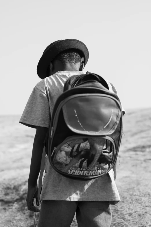 the back of the backpack is visible while a boy stands with a surfboard near water