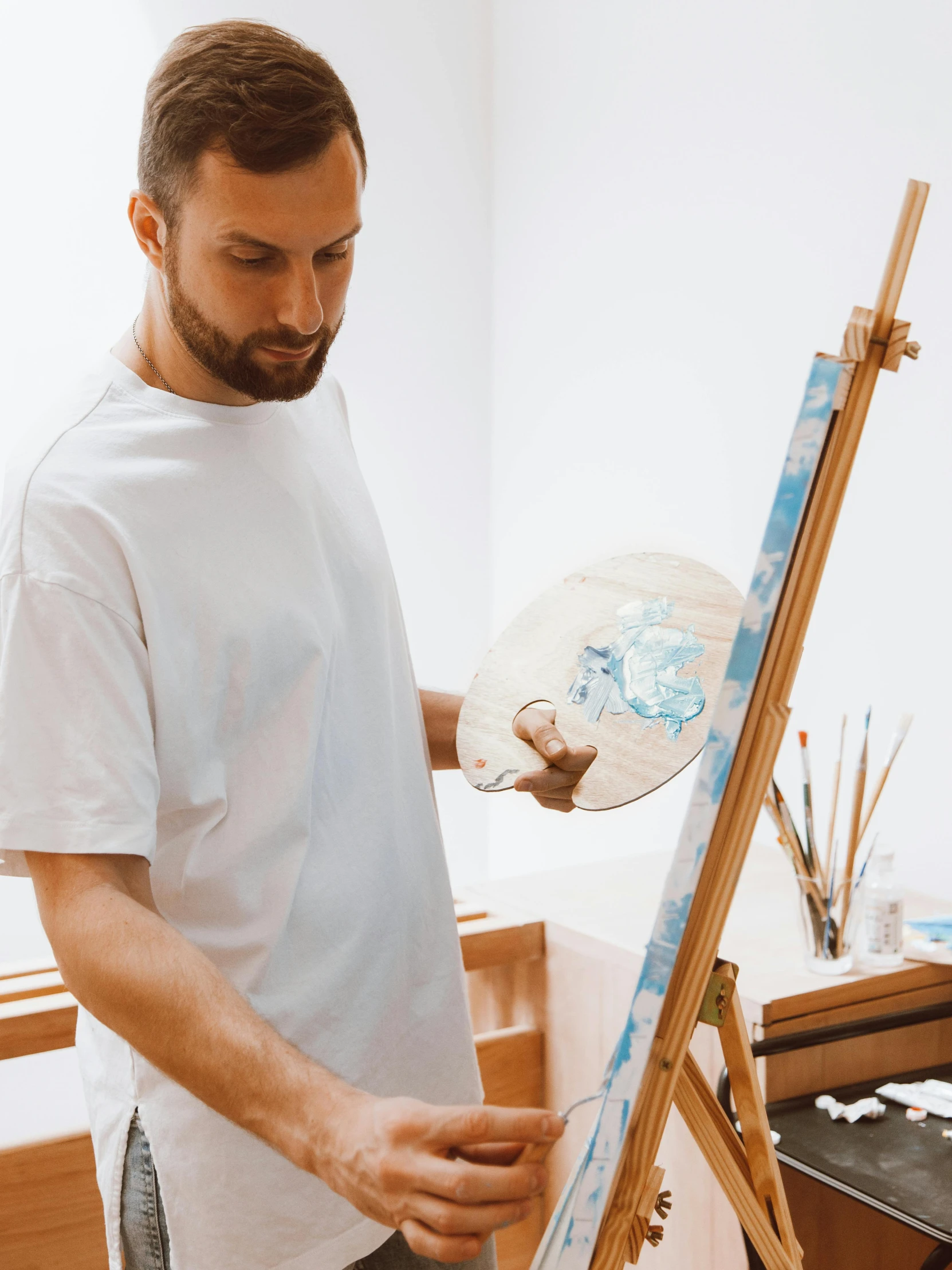 a man with a beard in front of a easel with brush and canvas