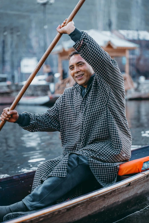 a man in a gray and black coat rowing a canoe