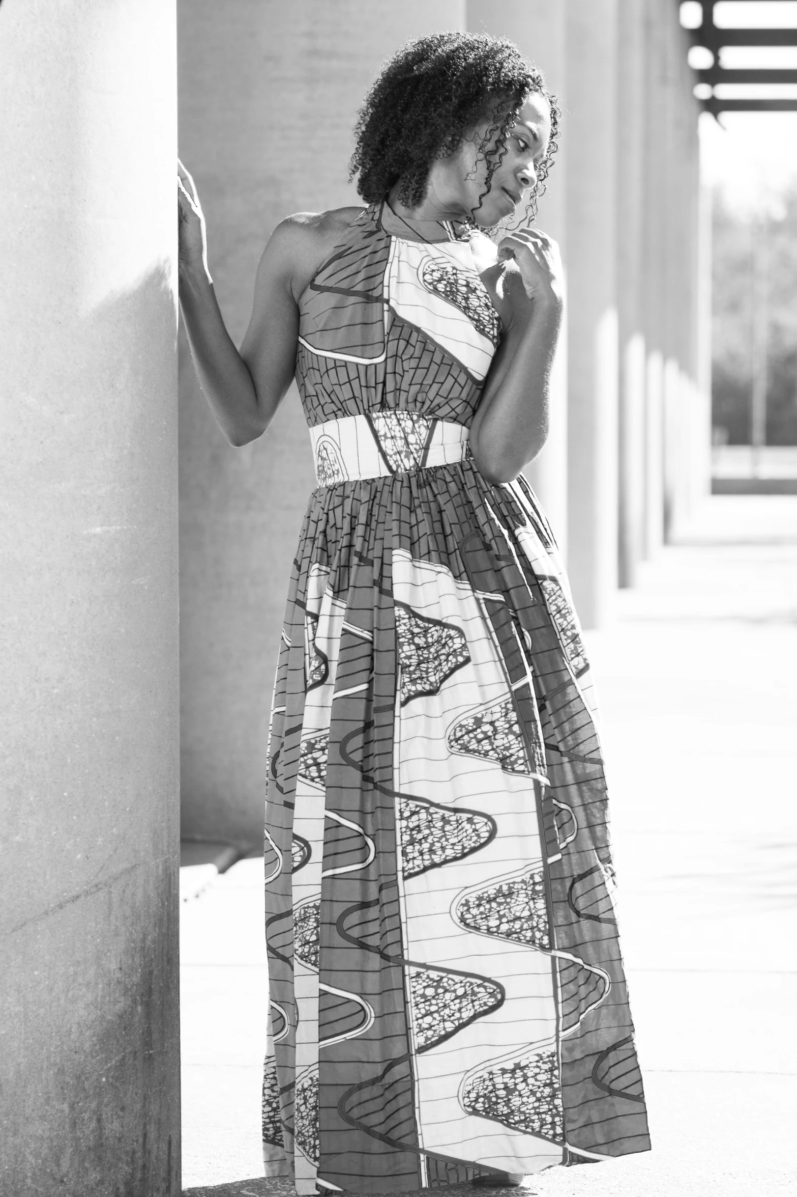 a black and white po of a woman in a dress leaning against a column