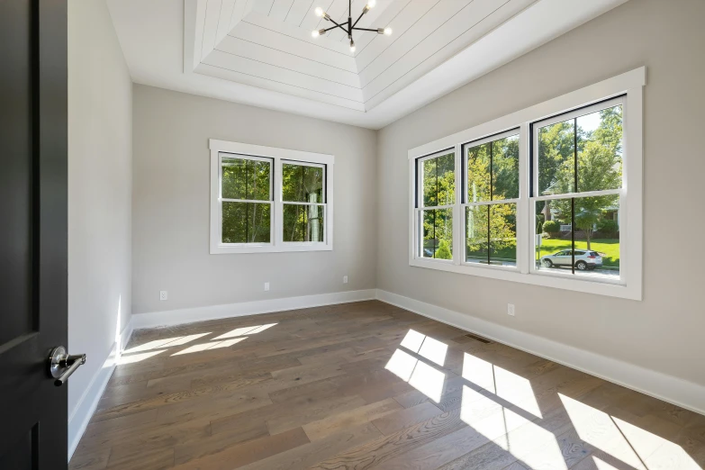 this is an empty room with two windows and hard wood floors