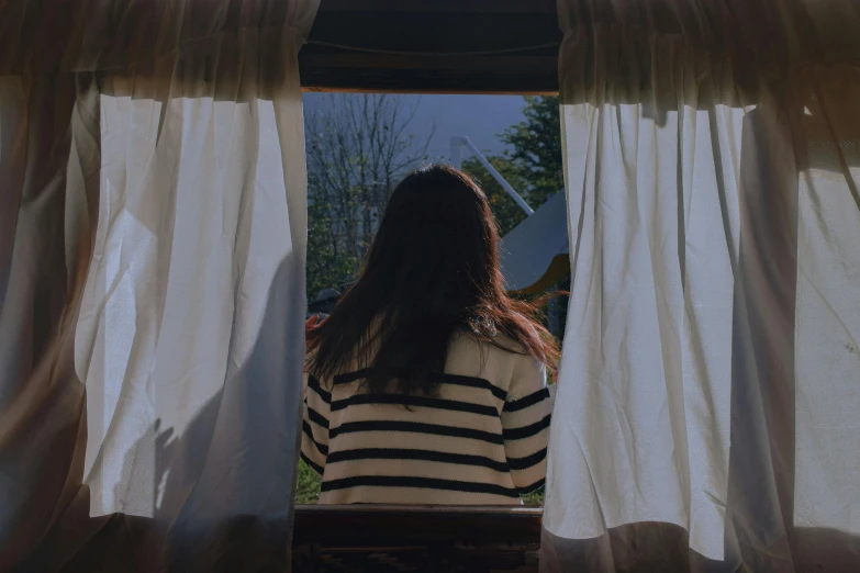 a young woman is sitting in front of the curtains in a house