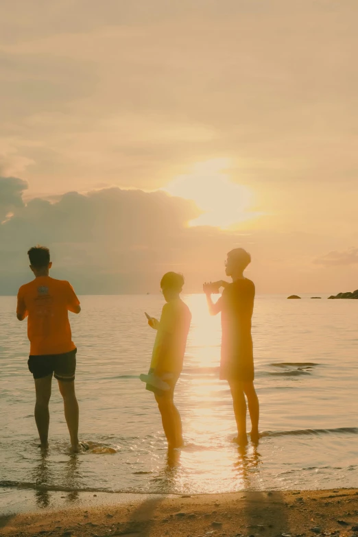 three young men standing in shallow water watching the sun go down