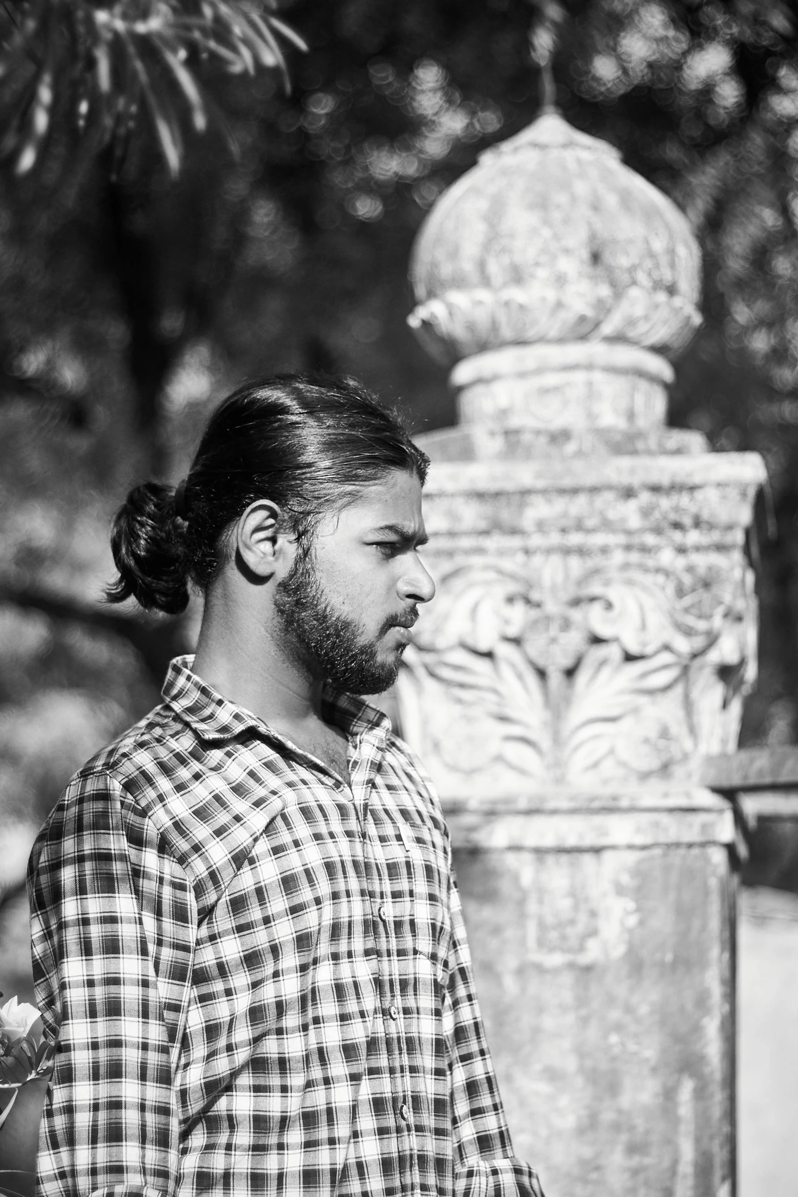 a man with a beard and a long bun in a shirt is standing near a statue