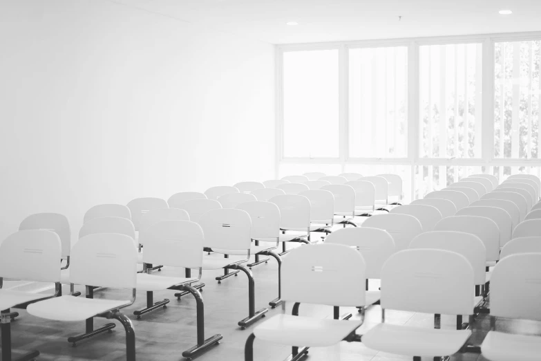 black and white po of rows of white classroom chairs in front of a big window