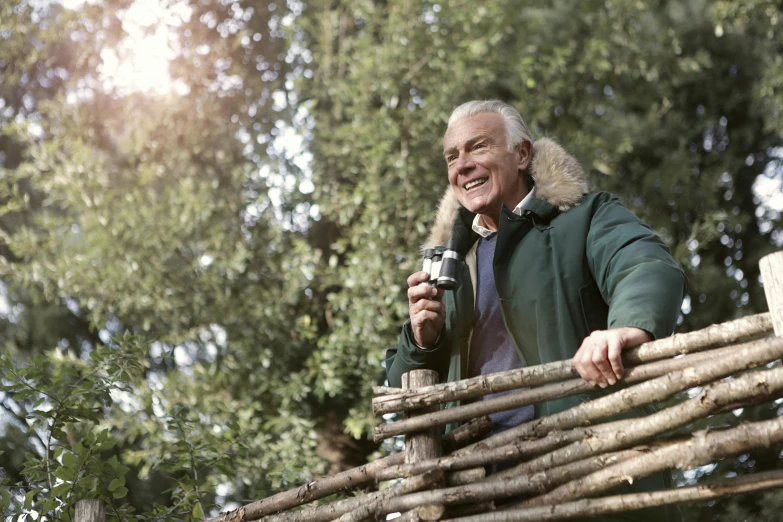 an old man holds a camera above the nches of a large set of wooden poles