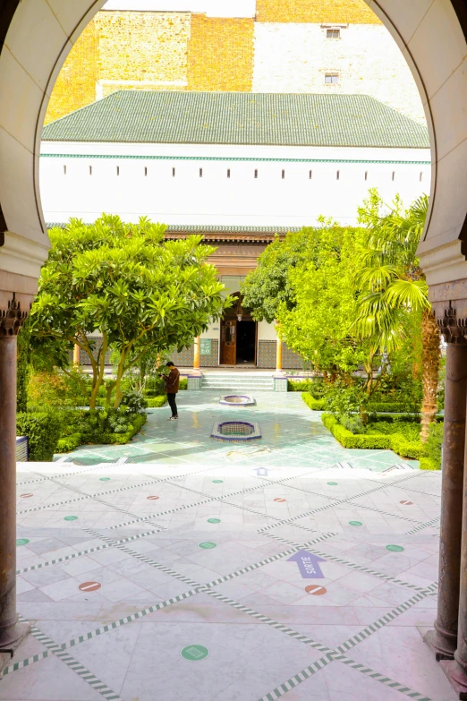 an arch leading into a building with green plants and white tiles on the floor