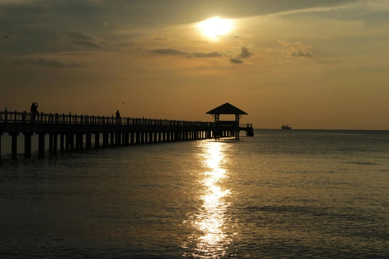 people stand on a pier and watch the sun set