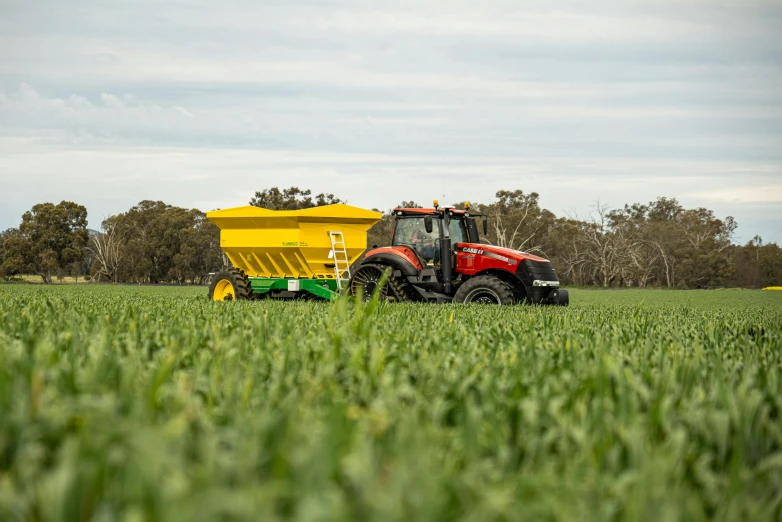 a farm tractor and a yellow trailer in a grassy field