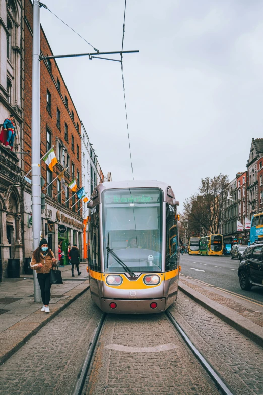 a silver bus traveling down train tracks next to tall buildings