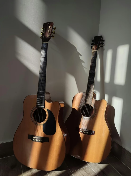 two guitars stand side by side in a corner