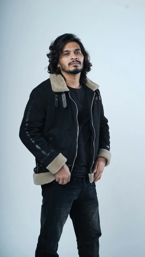 an indian man standing in a black jacket and jeans