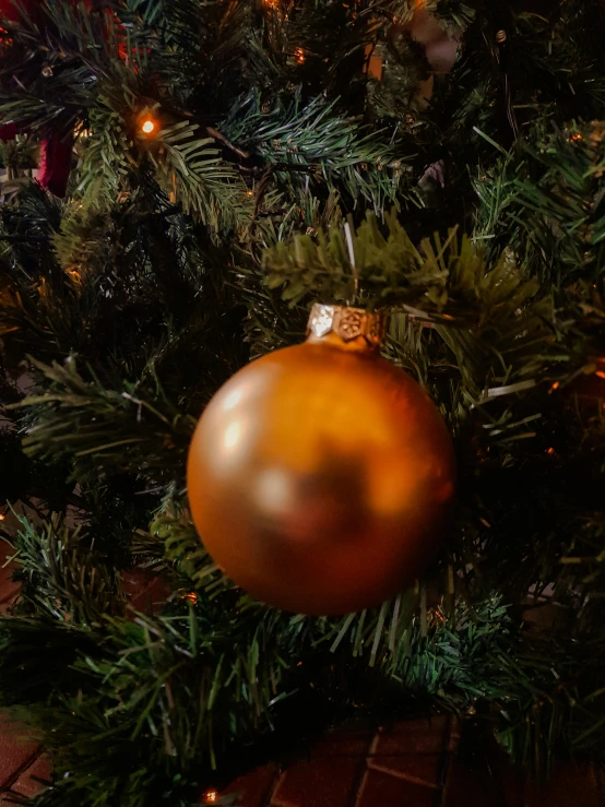 a gold christmas ornament hanging on a green tree
