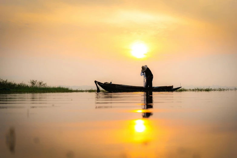 a person standing in a small boat at sunset