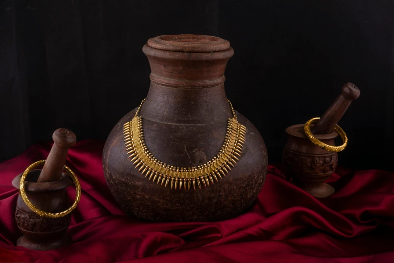 gold  necklaces on a brown vase and a red silk cloth